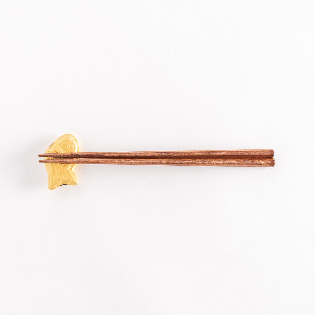 Wide shot showing a golden taiyaki-shaped chopstick rest with chopsticks placed across it.