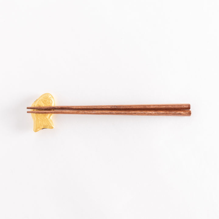 Wide shot showing a golden taiyaki-shaped chopstick rest with chopsticks placed across it.