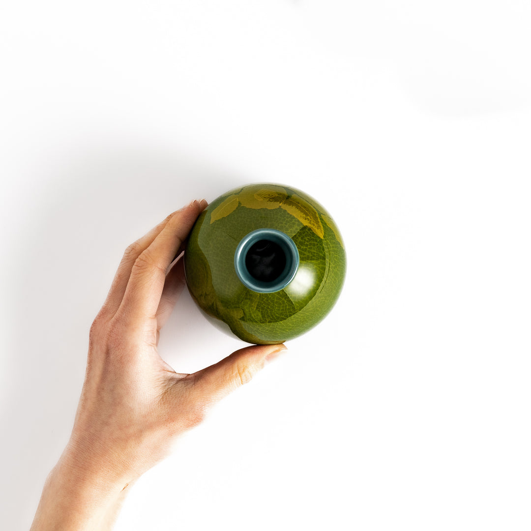 Hand holding a green ceramic sake carafe with a subtle leaf pattern, viewed from above, showcasing its elegant design and unique glaze.