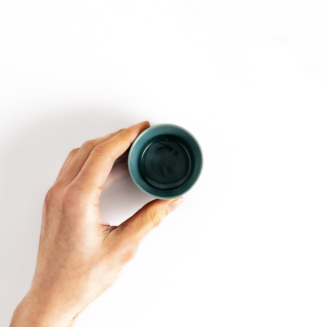 Hand holding a green sake cup with a smooth glaze, perfect for sipping and savoring the delicate flavors of sake.