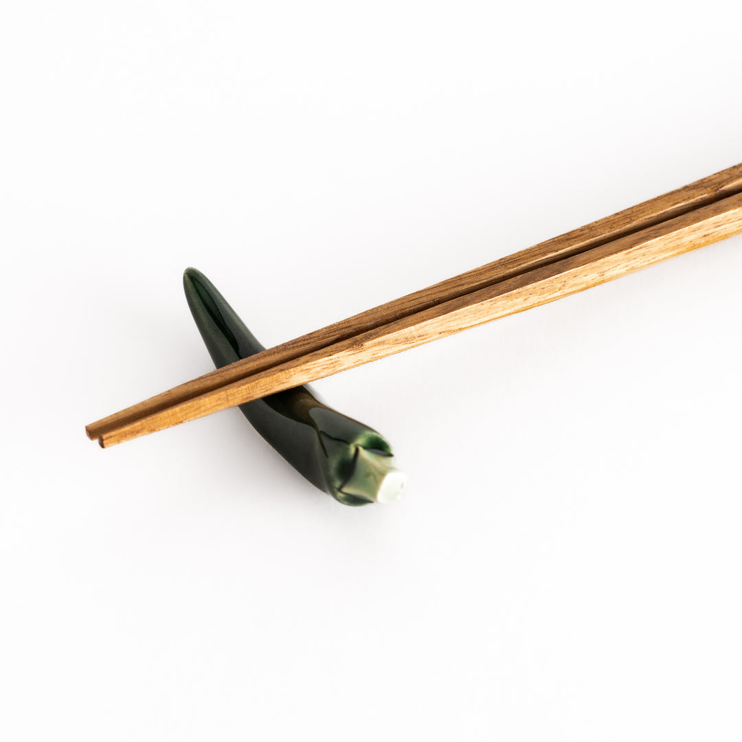 Close-up of chopsticks resting on the green chili pepper-shaped rest, emphasizing its detailed craftsmanship.