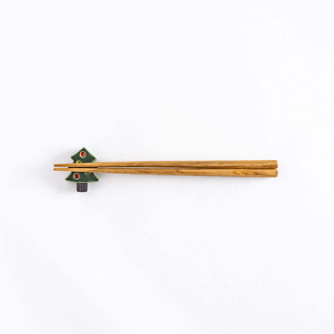 The green Christmas tree chopsticks rest with chopsticks resting on it, photographed from a distance.