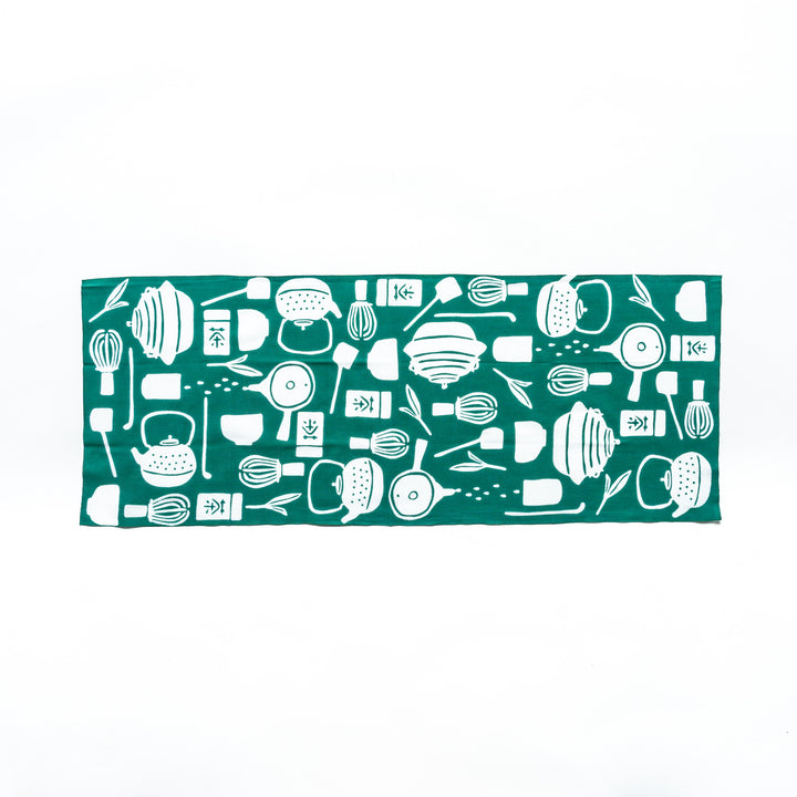 Fully opened dark green tenugui hand towel revealing white illustrations of teapots, whisks, and tea leaves.