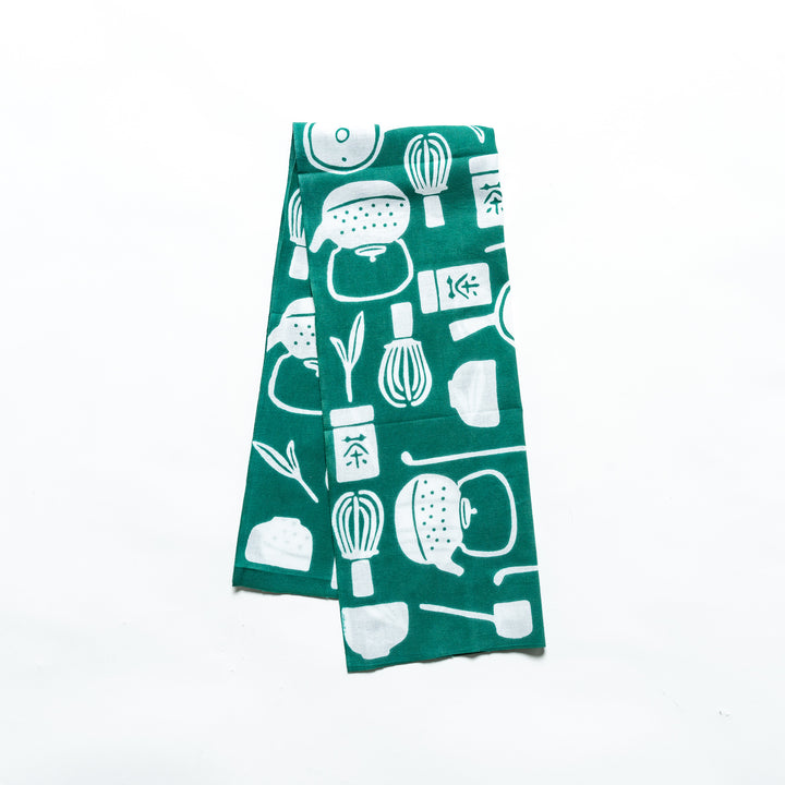 Dark green tenugui hand towel featuring white tea-themed illustrations, neatly folded and displayed.