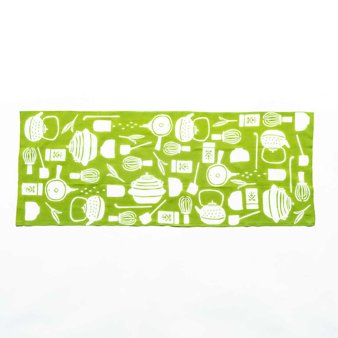 Light green tenugui hand towel laid flat, showing white teapots, tea leaves, whisks, and other tea-related designs.