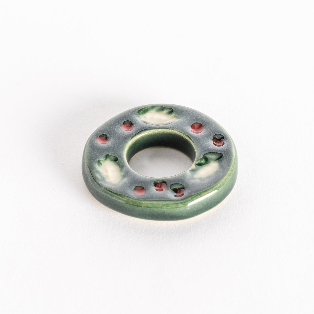 A slightly angled view of the ceramic green wreath chopstick rest, emphasizing its circular shape and glossy texture.