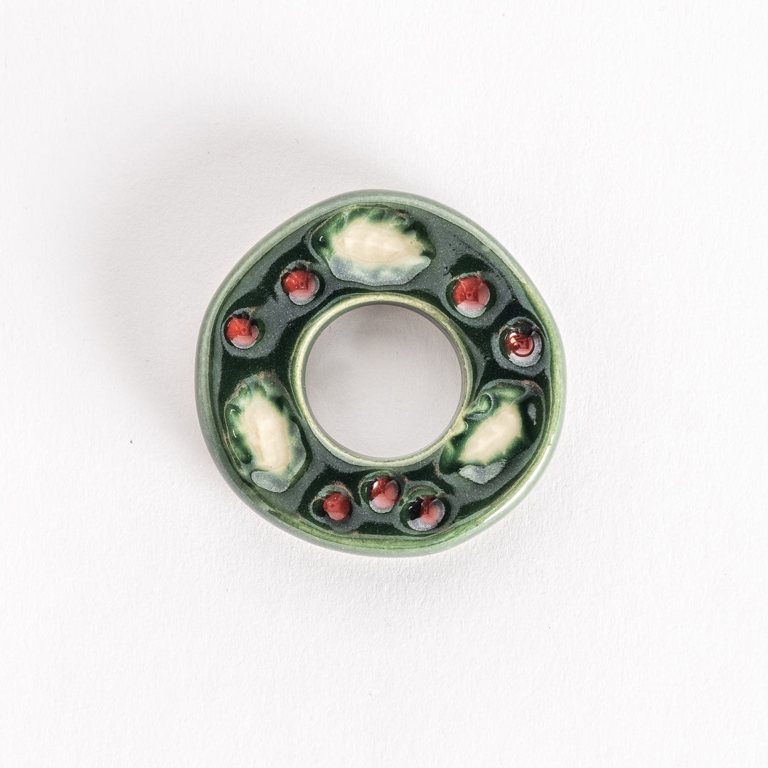 A ceramic chopstick rest shaped like a green wreath, featuring white accents and red berry details on a glossy finish.