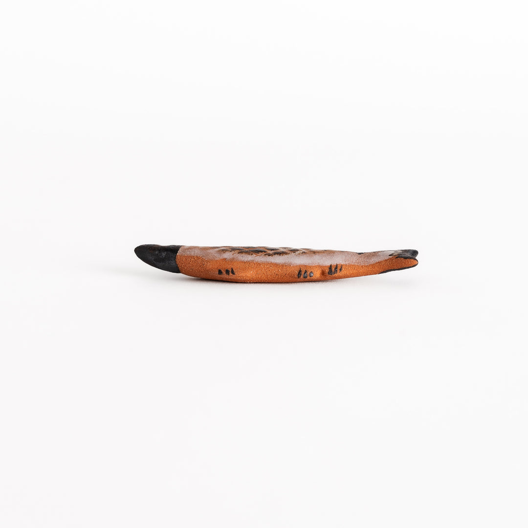 Side view of the grilled saury-shaped chopsticks rest, capturing its three-dimensional form and textured ceramic artistry.