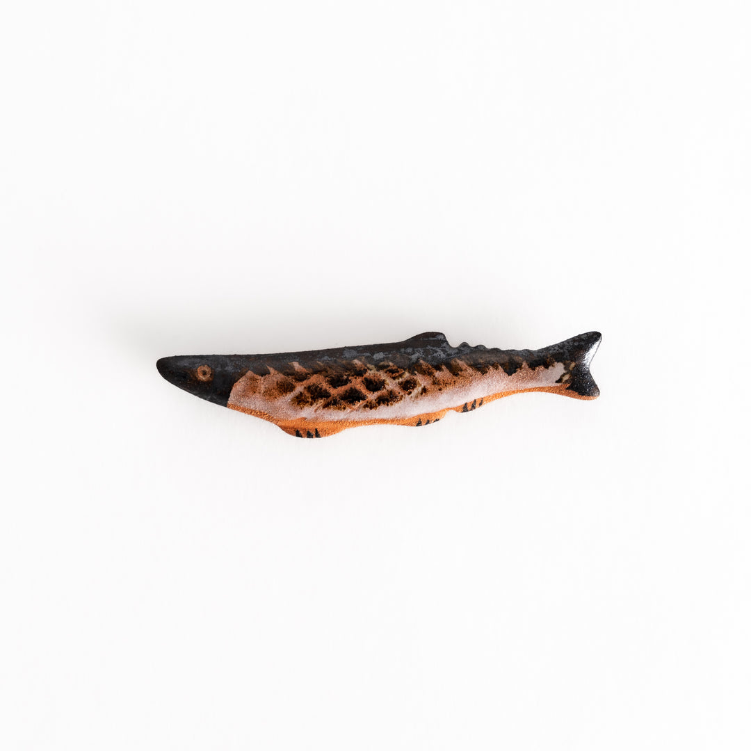 Ceramic chopsticks rest shaped like a grilled Pacific saury with textured scales and detailed black and brown glaze for a realistic finish.