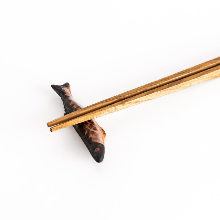 Close-up of chopsticks on the saury-shaped rest, highlighting the intricate texture and realistic color gradient of the fish design.