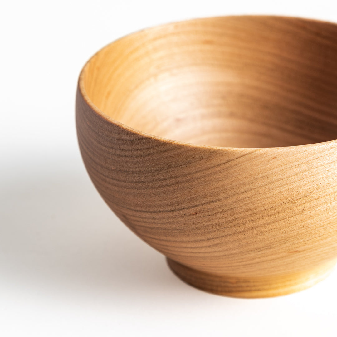 Side view of the cherry wood bowl, showcasing its gently curved edge and smooth finish. Warm, light wood tones.