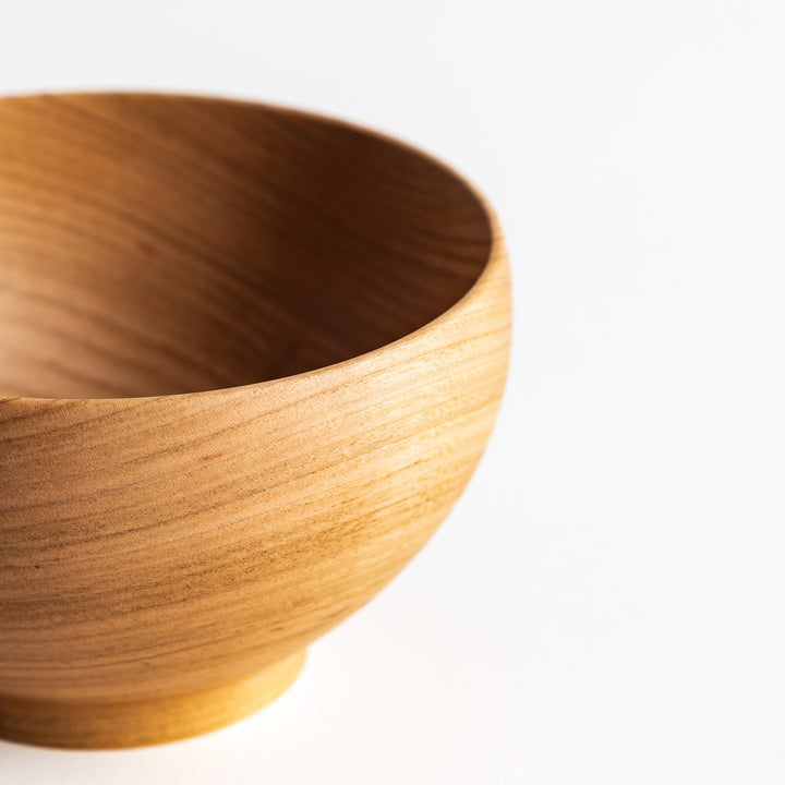 Angled view of the cherry wood bowl, emphasizing its smooth surface and beautiful wood grain. Simple, minimalist aesthetic.