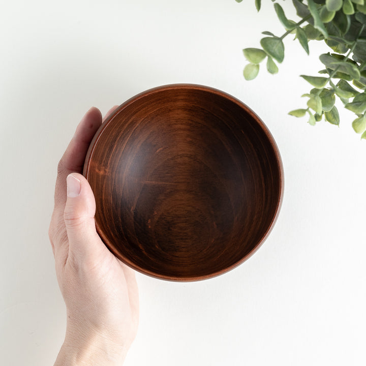 Hand holding the dark brown cherry wood bowl, showcasing the inner grain pattern and bowl’s depth.