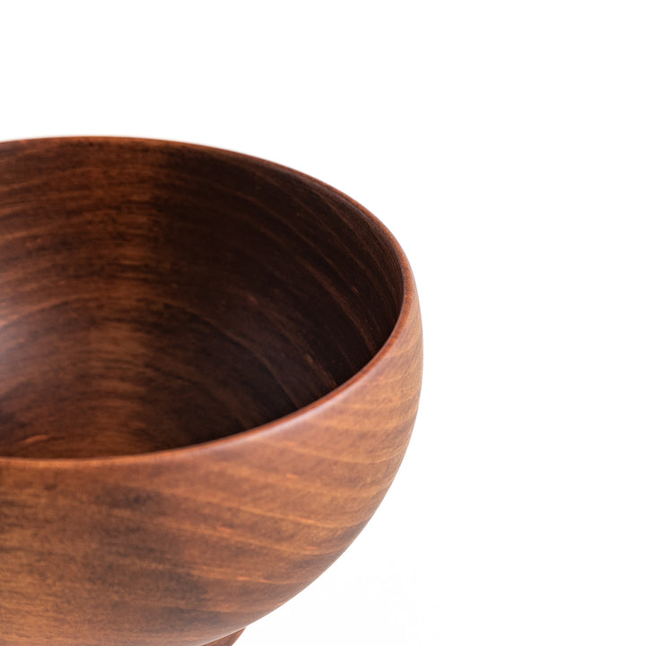 Angled view of the dark brown cherry wood bowl’s side, displaying its gentle curves and grain detail.