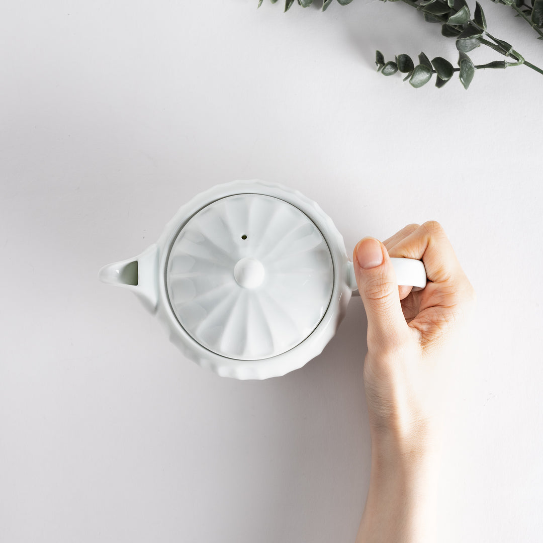 Close-up of the teapot held in hand, emphasizing the intricate petal details and elegant shape for tea enjoyment.