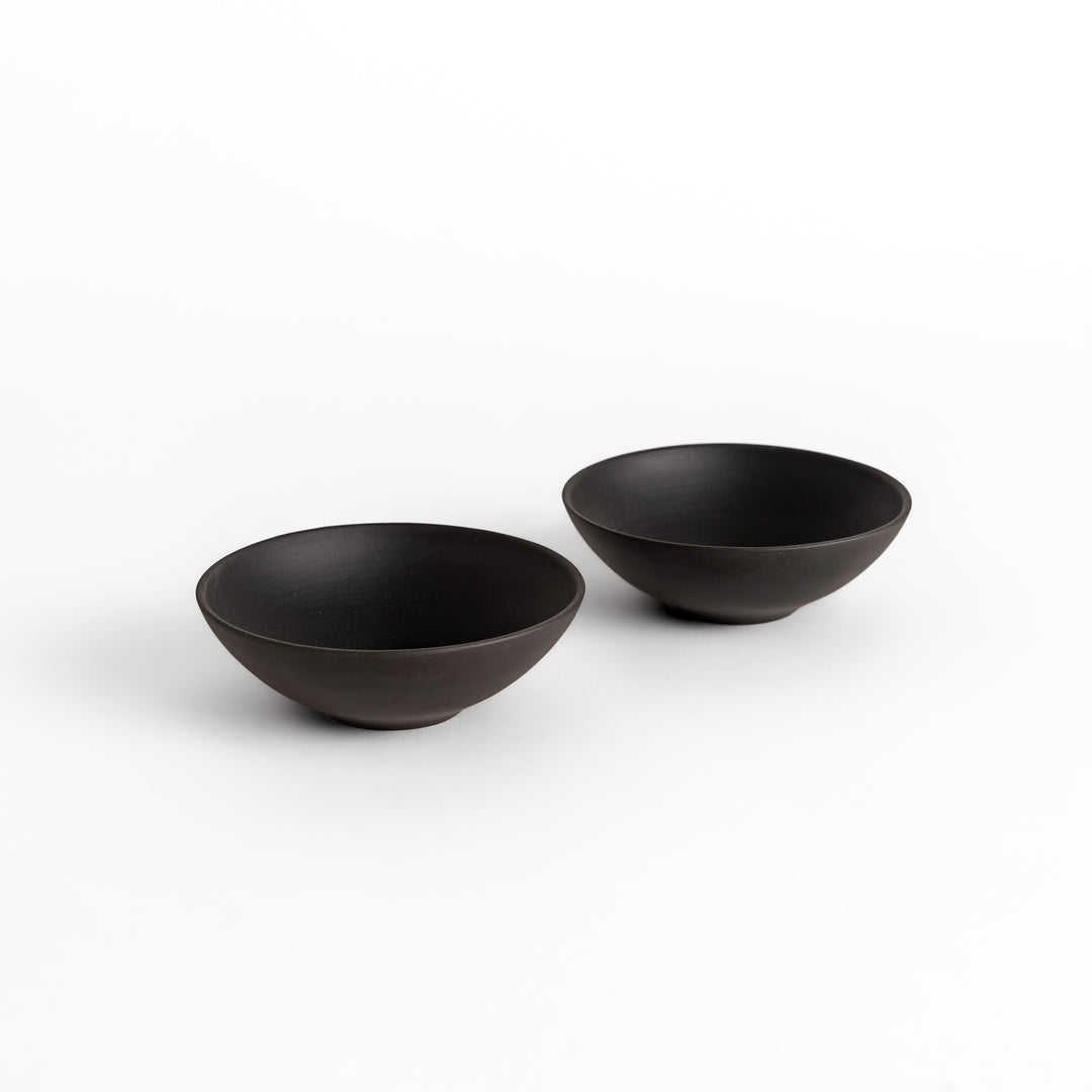 Two minimalist black teacups with a matte finish, elegantly paired as a set for a refined tea-drinking experience.