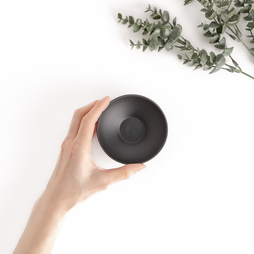 Top-down view of a black teacup with a hand holding it, showcasing its simple and ergonomic design.