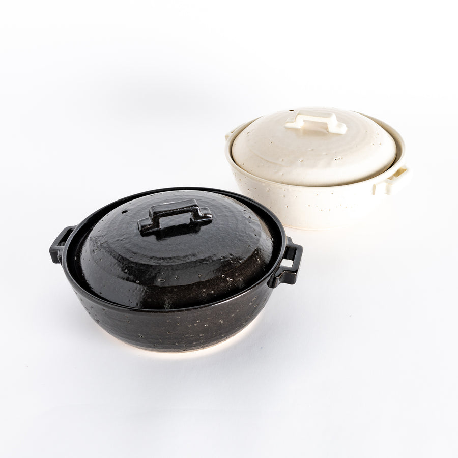 Two donabe pots side by side: one with a glossy black glaze and the other in a smooth, off-white finish, both featuring square handles and lids.