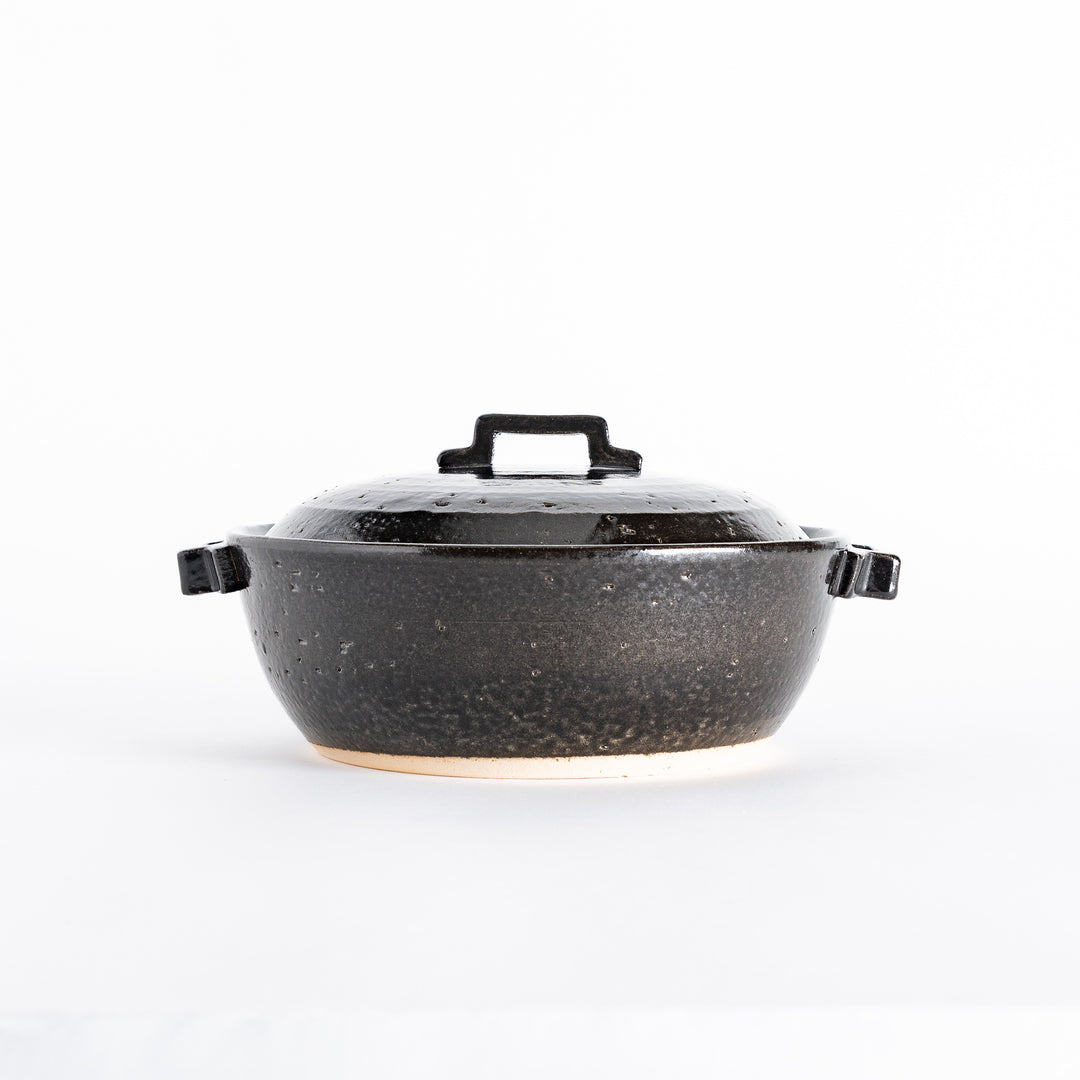 Side view of a black donabe pot with a rounded shape and sturdy handles, set against a clean background.