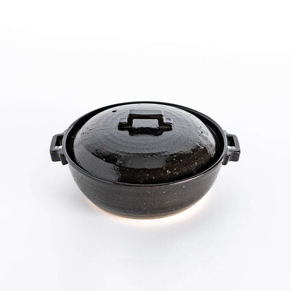 A glossy black donabe pot with a square handle and smooth finish, showcasing its modern design.