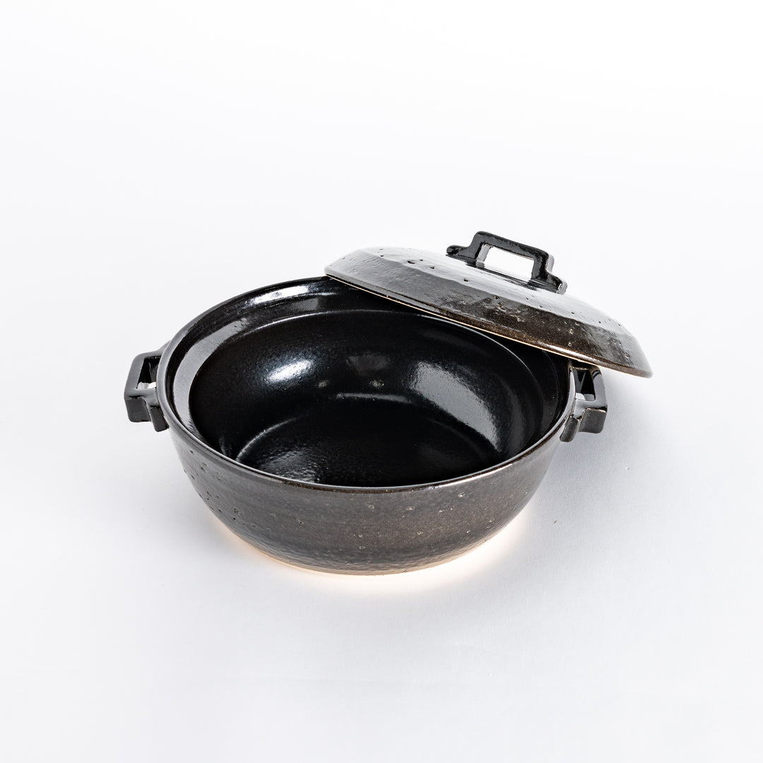 Black donabe pot with the lid slightly shifted, revealing the smooth interior of the pot.