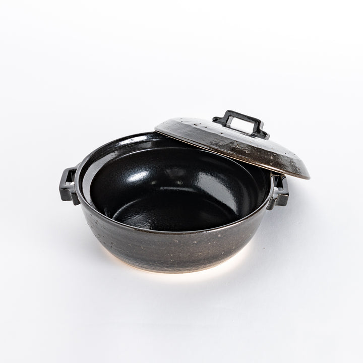 Black donabe pot with the lid slightly shifted, revealing the smooth interior of the pot.