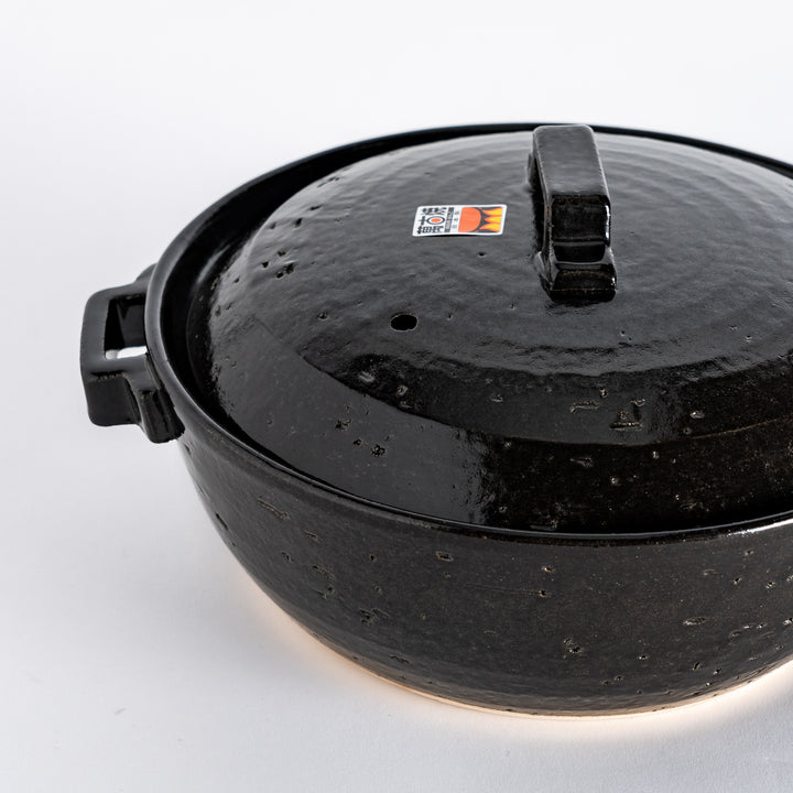 Close-up of the black donabe pot's glossy surface and textured details near the square lid handle.