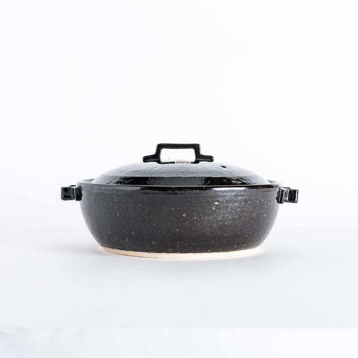 Side view of a black donabe pot with a rounded shape and sturdy handles, set against a clean background.