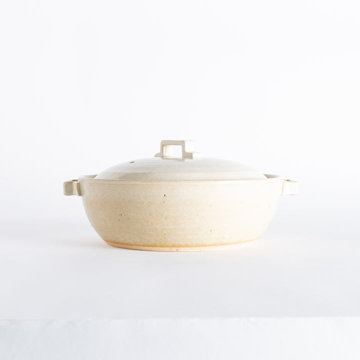 Side view of an off-white donabe pot with a rounded design, soft speckled details, and sturdy handles.