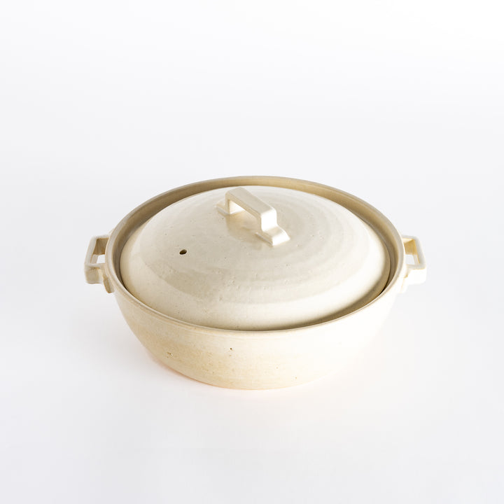 An off-white donabe pot with a subtle speckled finish and square handle, reflecting a simple and elegant style.