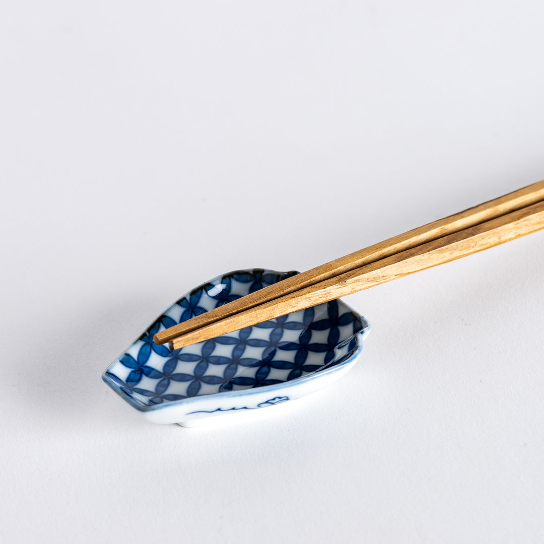 A pair of wooden chopsticks resting on a small blue geometric-patterned sauce dish shaped like a vase.