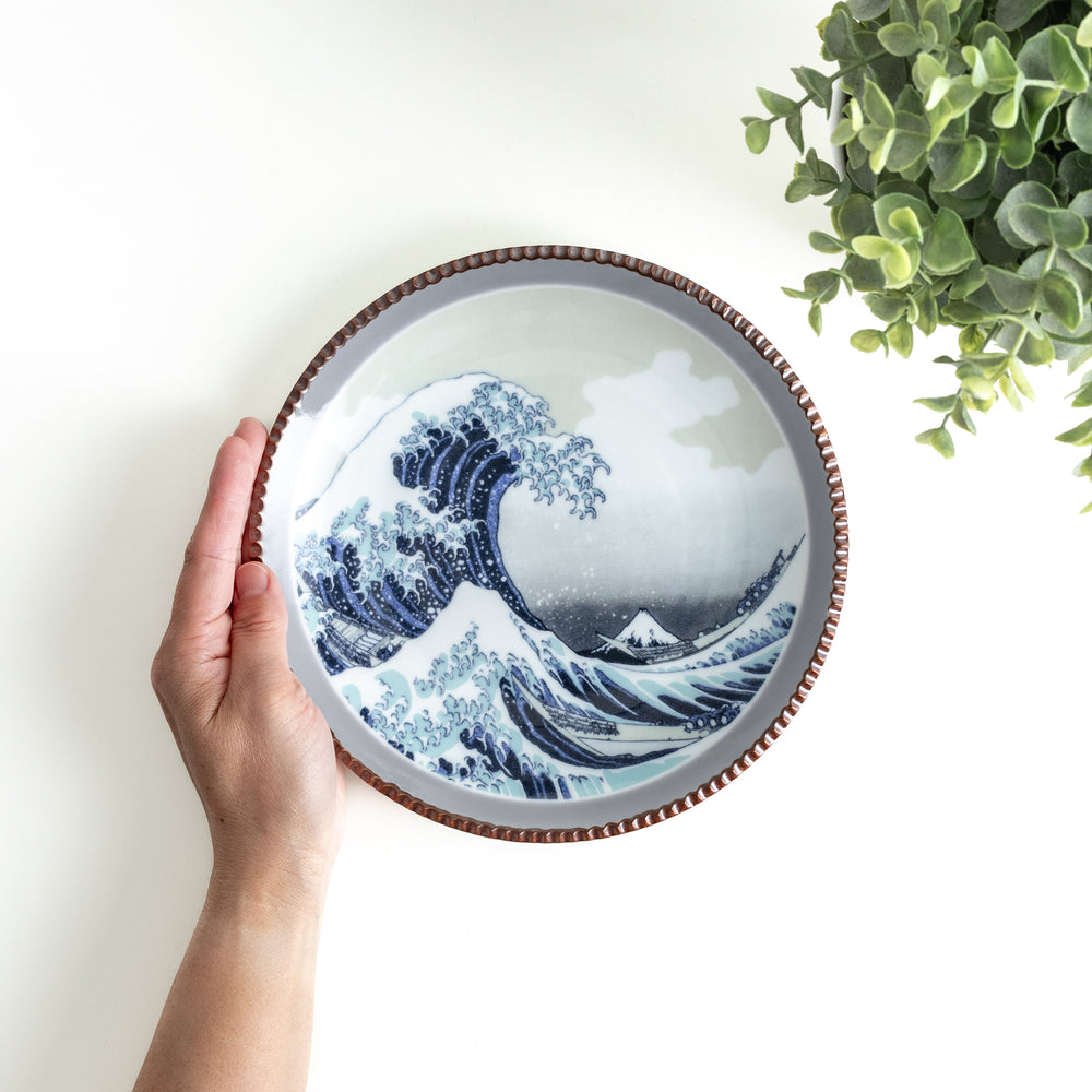 Hand holding a beautiful salad plate featuring Hokusai's iconic Great Wave design with a unique hammered copper rim.