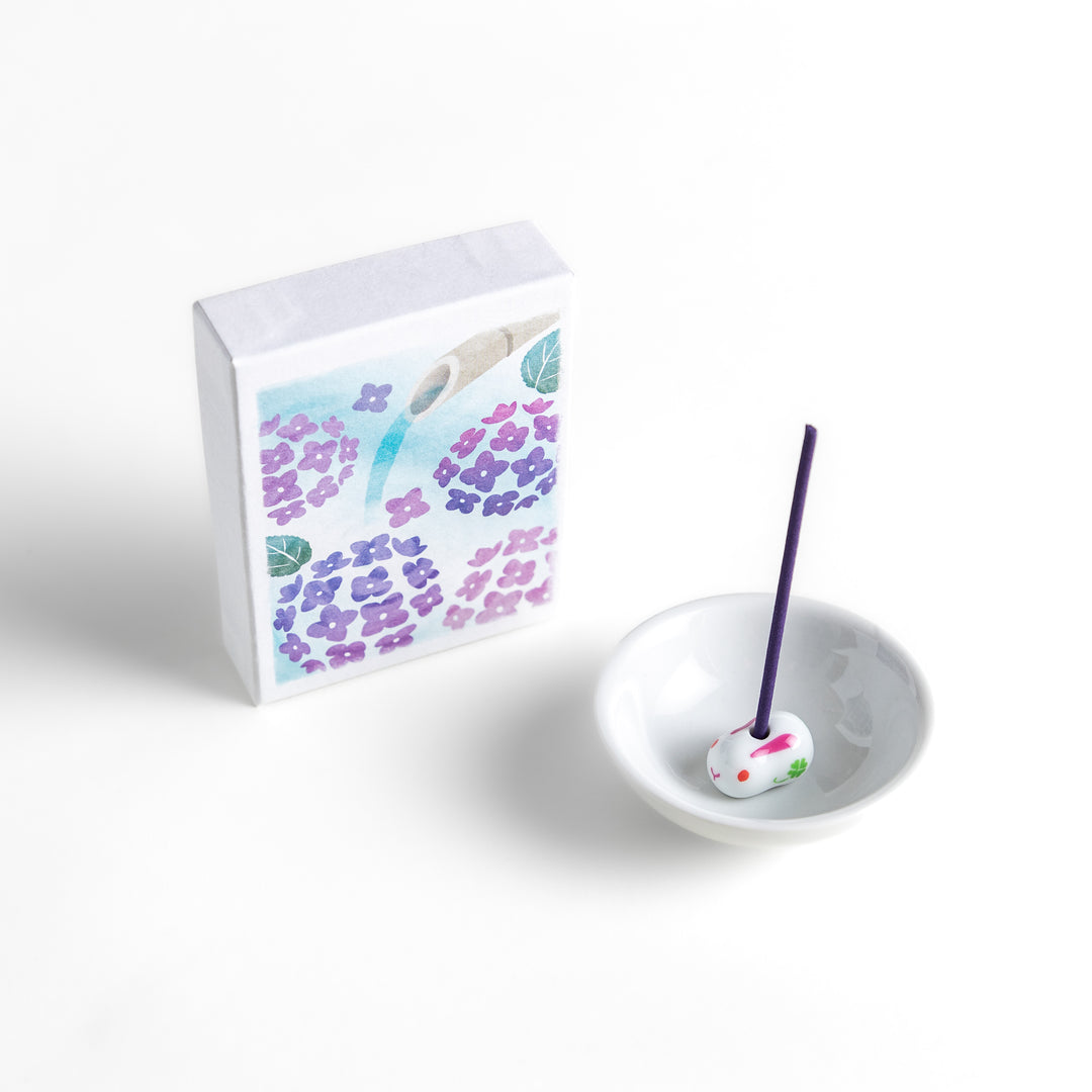 Incense with deep purple sticks, presented in a box adorned with delicate hydrangea flowers and a flowing bamboo spout, offering a serene and refreshing floral fragrance.