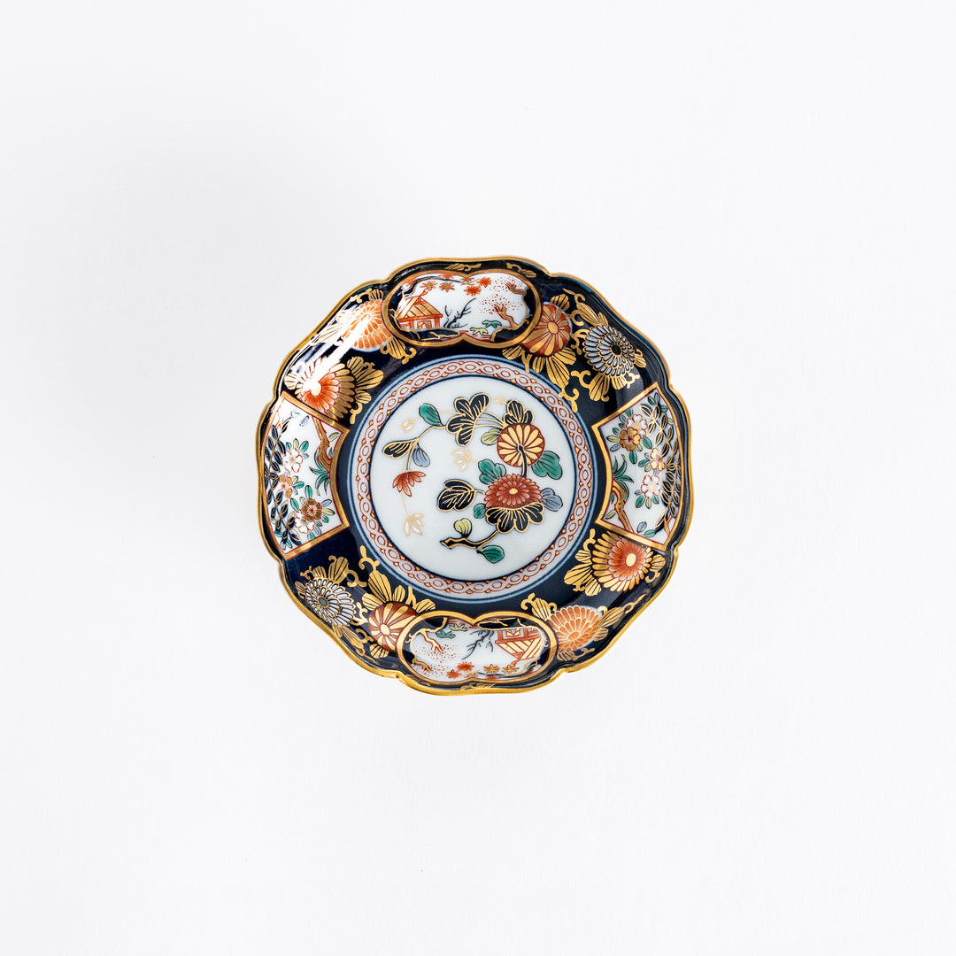 Top view of a delicate sauce dish featuring intricate floral patterns in vibrant colors of red, gold, and green, set against a dark blue background with gilded details.