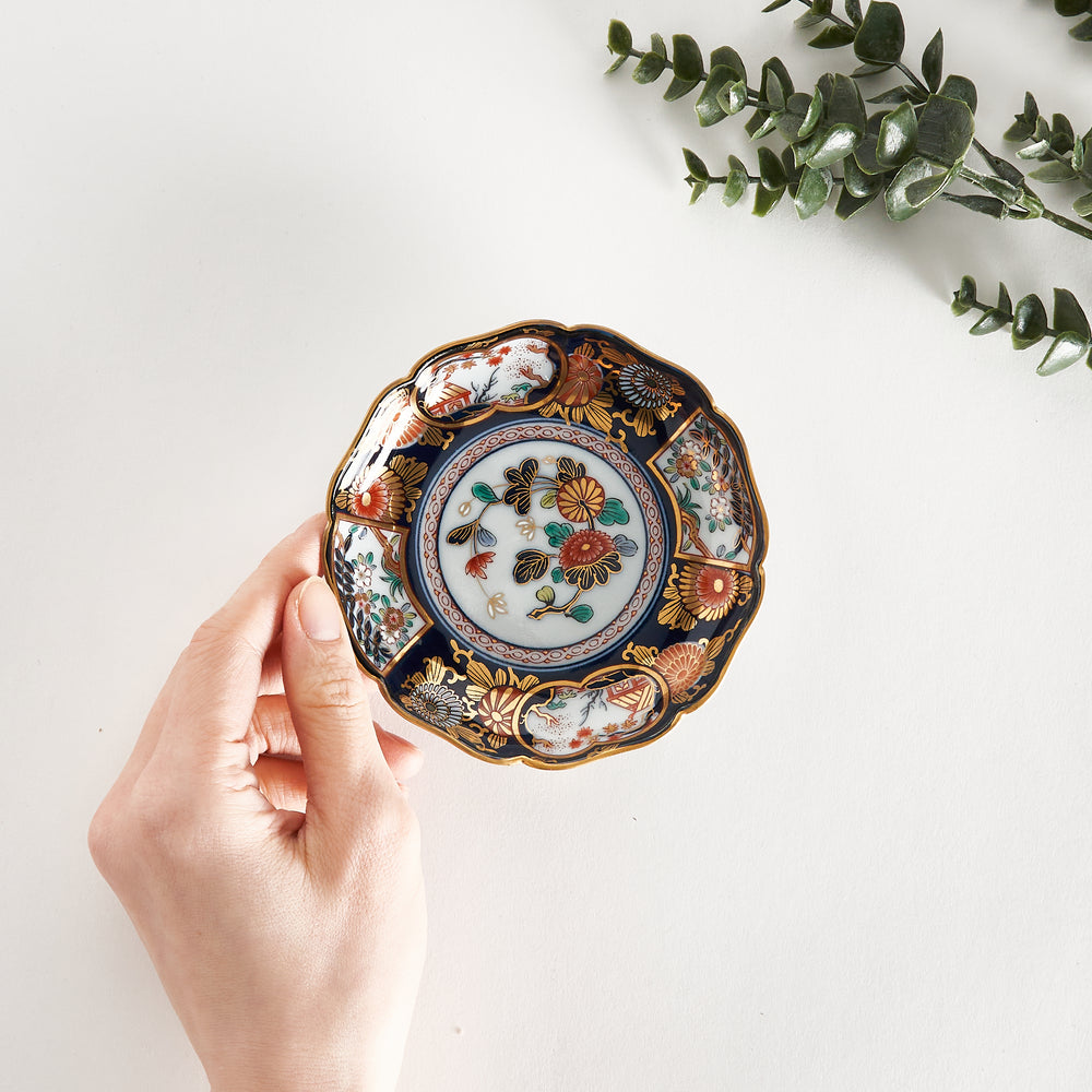 Hand holding an ornate Imperial Blossom Sauce Dish with intricate gold, red, and green floral patterns on a deep navy base.