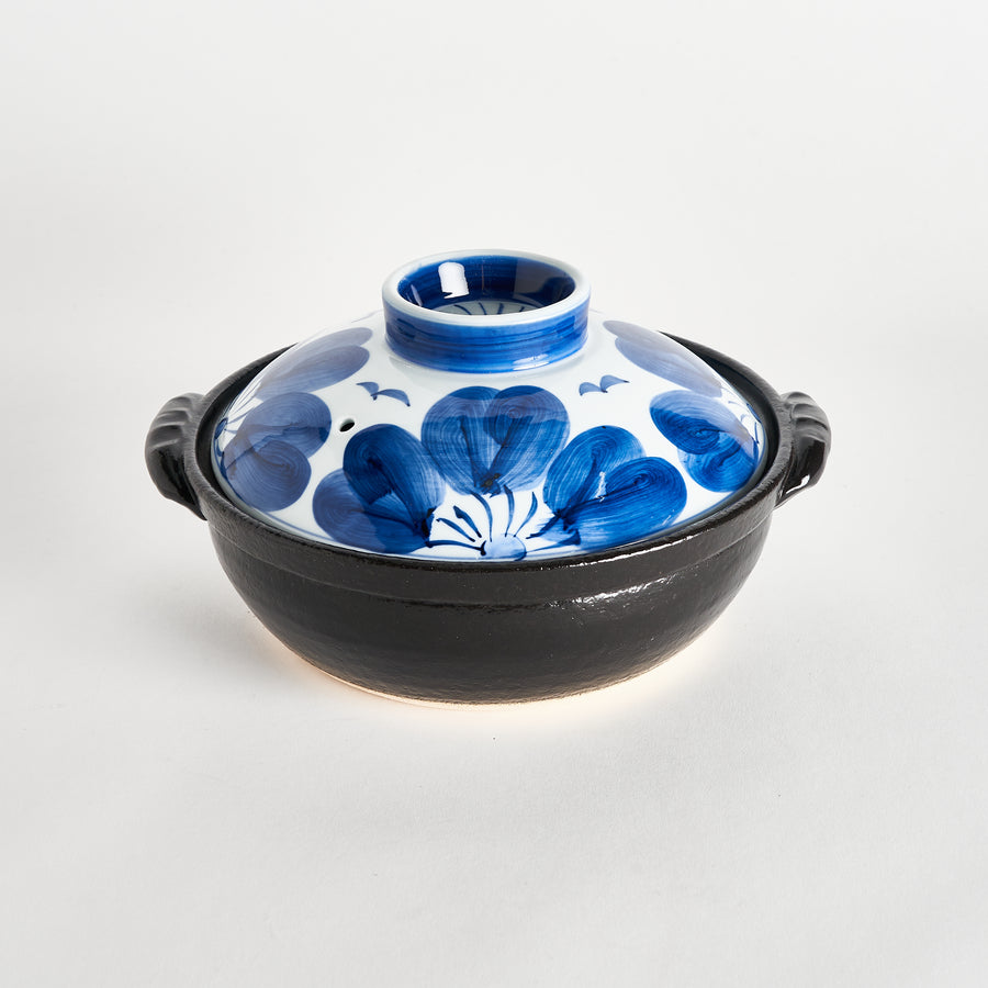 A round donabe with a black ceramic base and a lid featuring a large blue flower design. It has a small hole for ventilation.