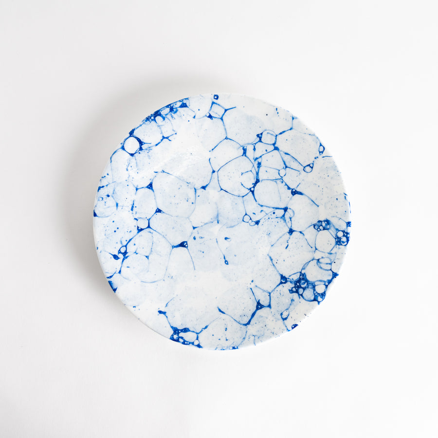 A round dinner plate with a blue bubble-like design on a white background.