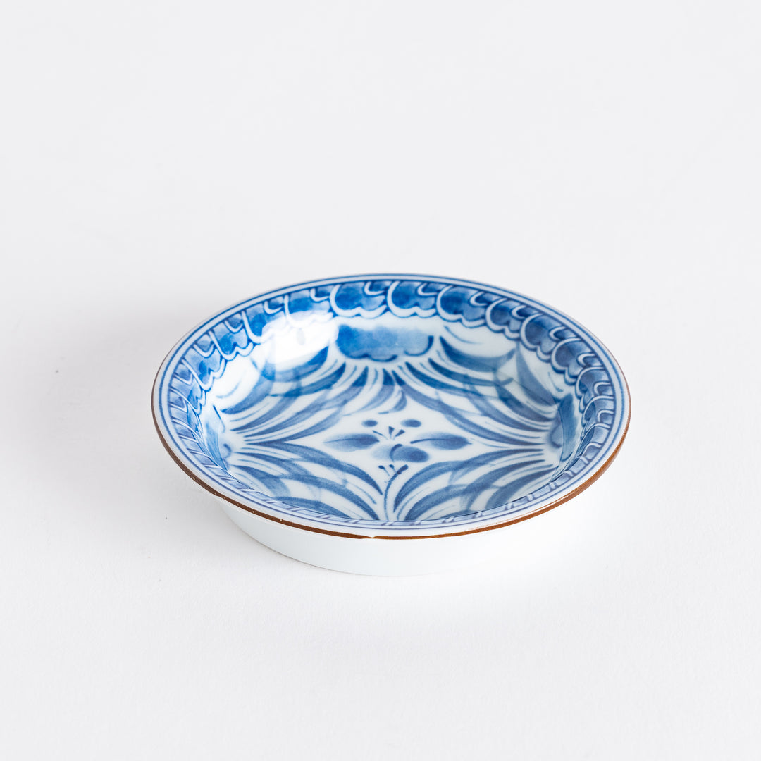 A side view of the Iris Arabesque sauce dish, featuring intricate blue arabesque patterns inside with a soft scalloped rim. The dish has a subtle brown border accent.