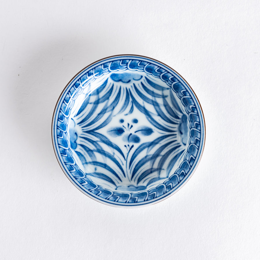 Small round dish featuring an intricate blue iris arabesque pattern on a white background, showcasing fine detailing and elegant curves.