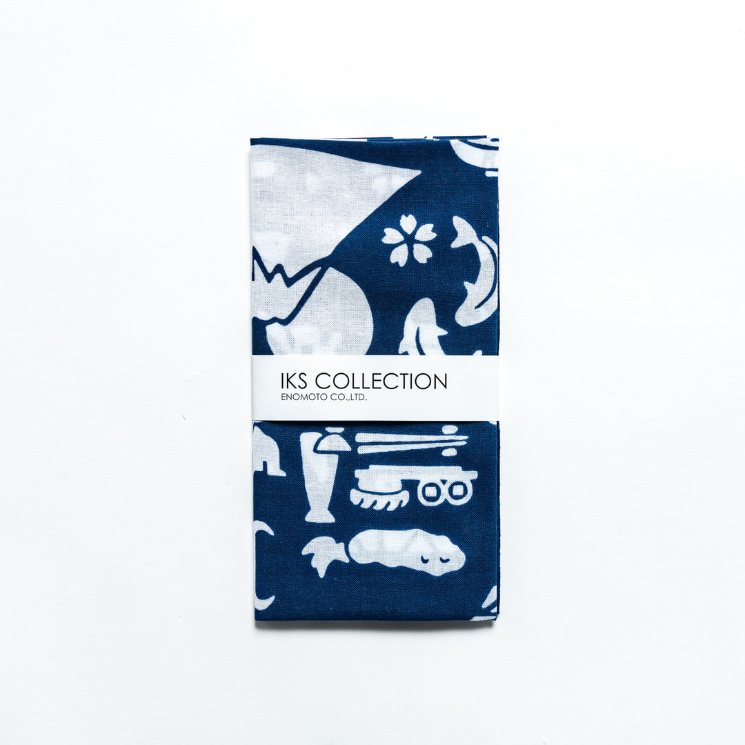 Folded dark blue tenugui with Japanese icon patterns, secured with a branded sleeve.