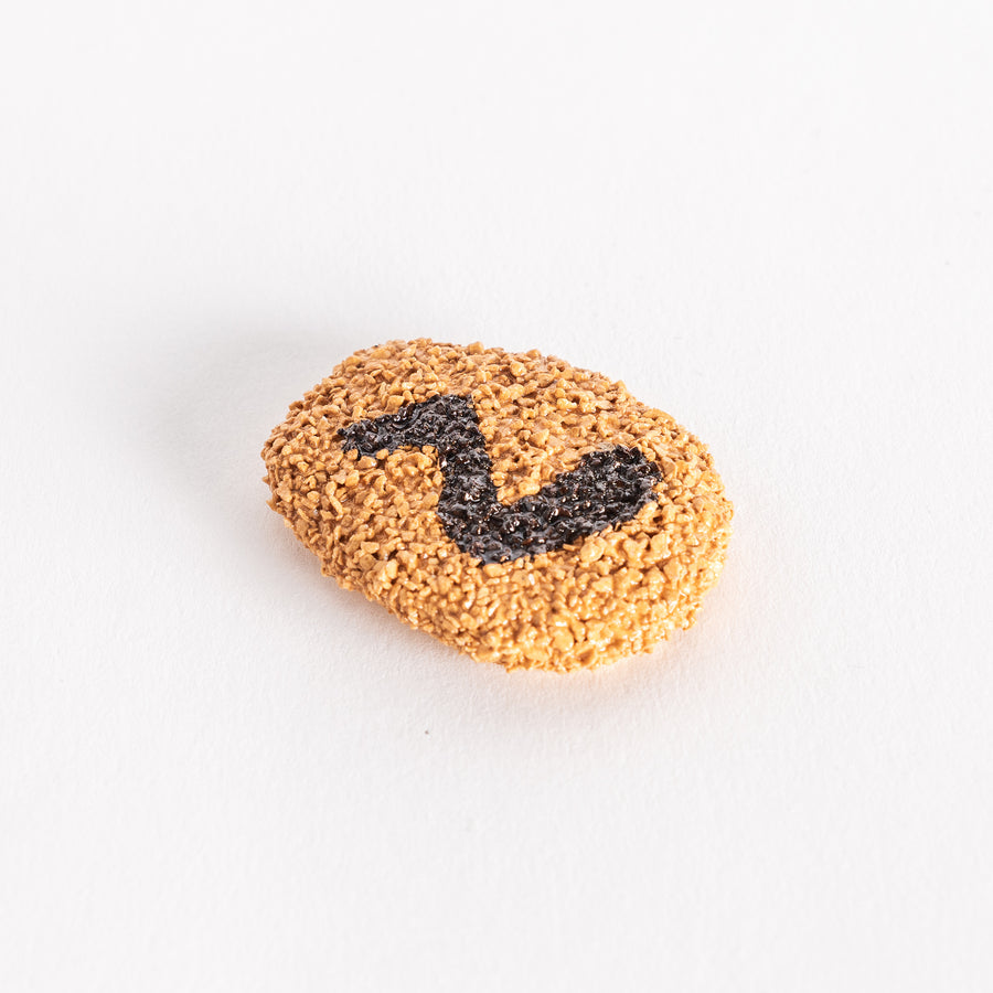 Close-up view of a chopstick rest shaped like a Japanese croquette, featuring a golden breadcrumb texture and a black swirl design on top.