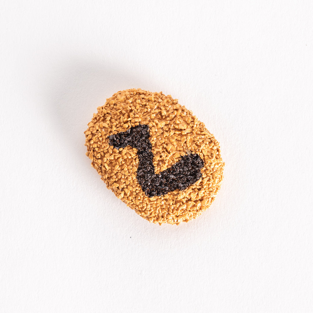 Slightly angled view of a chopstick rest shaped like a Japanese croquette, with its crumbly texture and prominent black swirl decoration clearly visible.