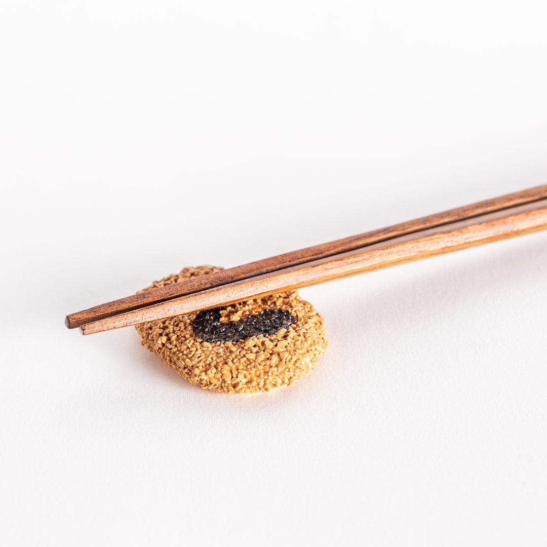 View of a Japanese croquette-shaped chopstick rest with chopsticks placed on top, showing the textured surface and distinct black swirl design.