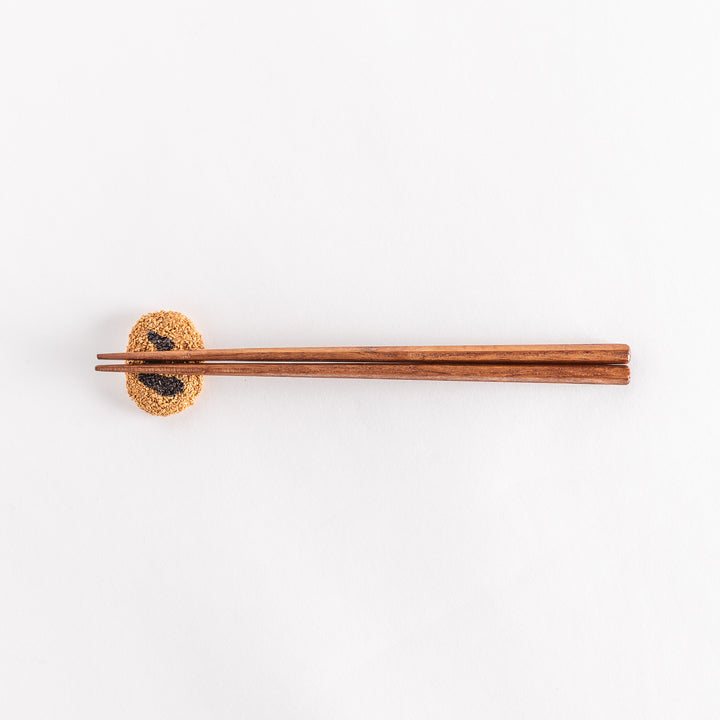 A wider-angle view of a Japanese croquette-shaped chopstick rest with chopsticks placed on top, showing the textured breadcrumb surface and black swirl design.