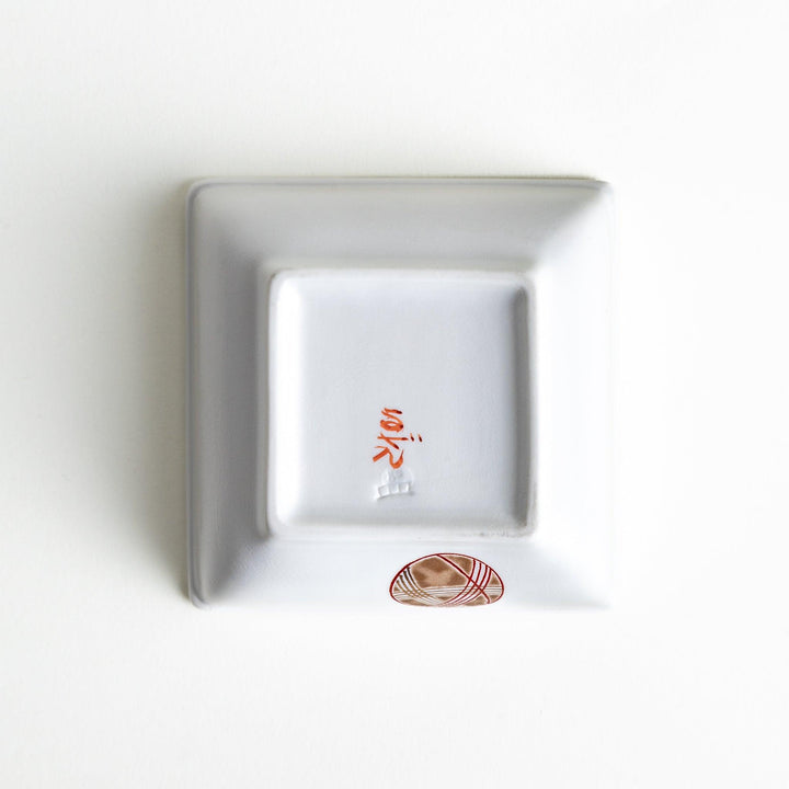 A white square bowl decorated with red and gold circular patterns.