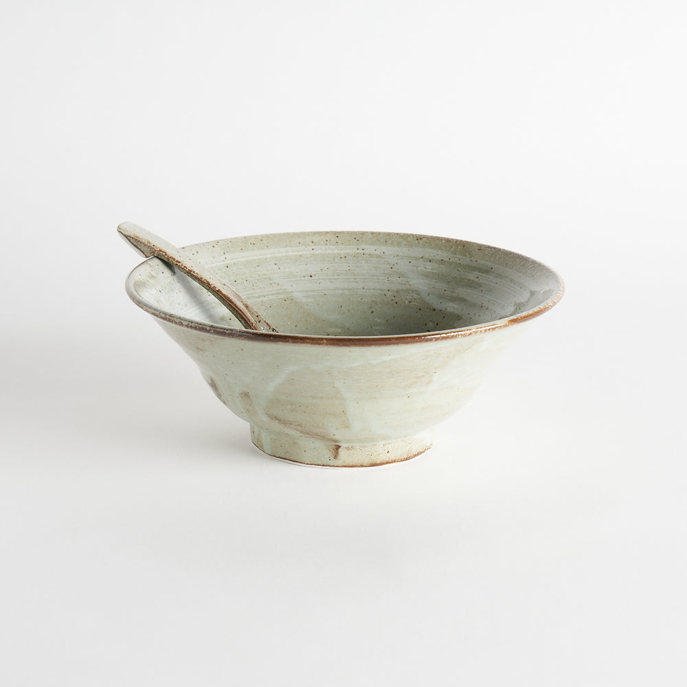 A hand holding a whale and wave patterned ramen bowl and spoon, with additional bowls in the background.