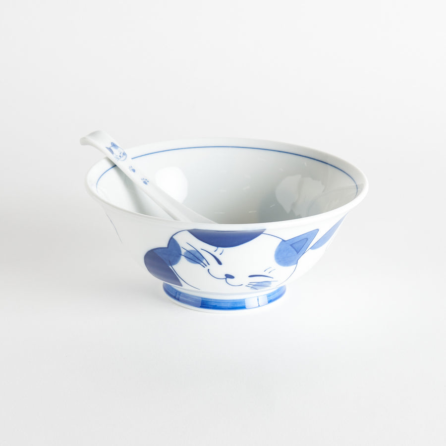 A blue and white ramen bowl with a cute cat face design, accompanied by a matching spoon.