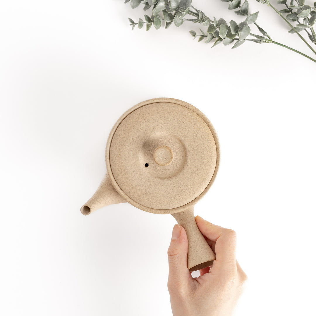 Top-down view of the beige teapot with a hand on the handle, showcasing its functional and ergonomic design.