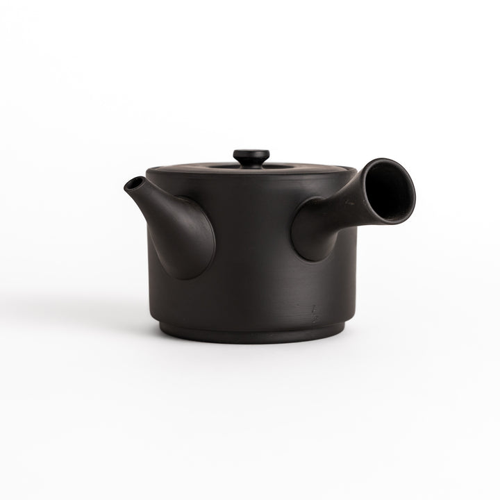 Modern black teapot with a round body, horizontal spout, and lid, crafted from textured ceramic for a minimalist tea experience.