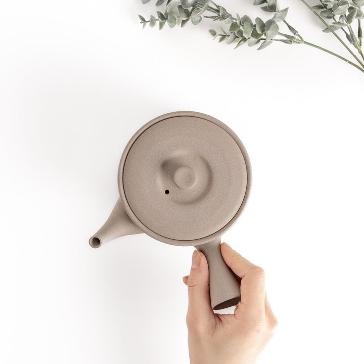 Top-down view of the gray teapot with a hand on the handle, showcasing its functional and ergonomic design.